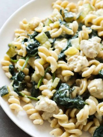 Boursin pasta with spinach and chicken on a white plate.