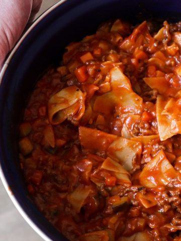 Lasagnette bolognese in a blue pan held by a man.