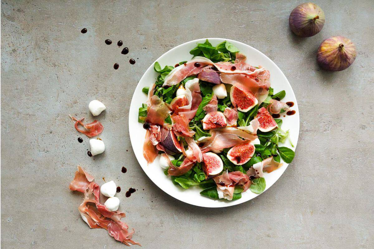 Fig salad with arugula and prosciutto on a plate.