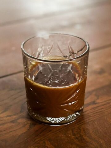 Dark caramel sauce in a glass on a wooden table.