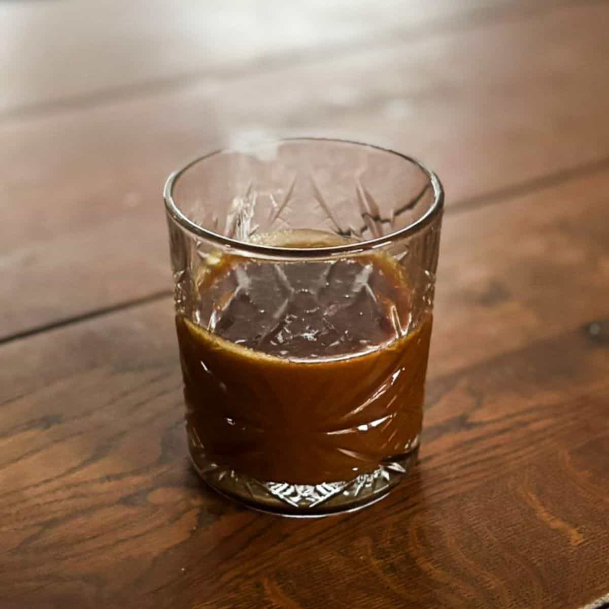 Dark caramel sauce in a glass on a wooden table.